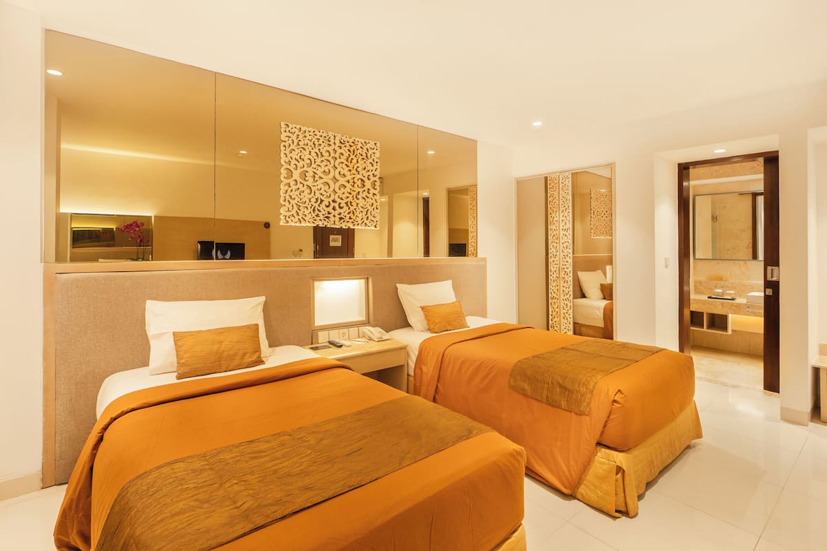A hotel room with two beds, a large mirror, a nightstand, and a bathroom visible through an open door.