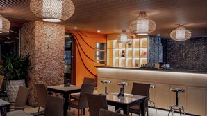 A modern restaurant with wicker chairs, a stone pillar, and a bar area with a counter and shelves. - Kuta Angel Hotel (Kuta)