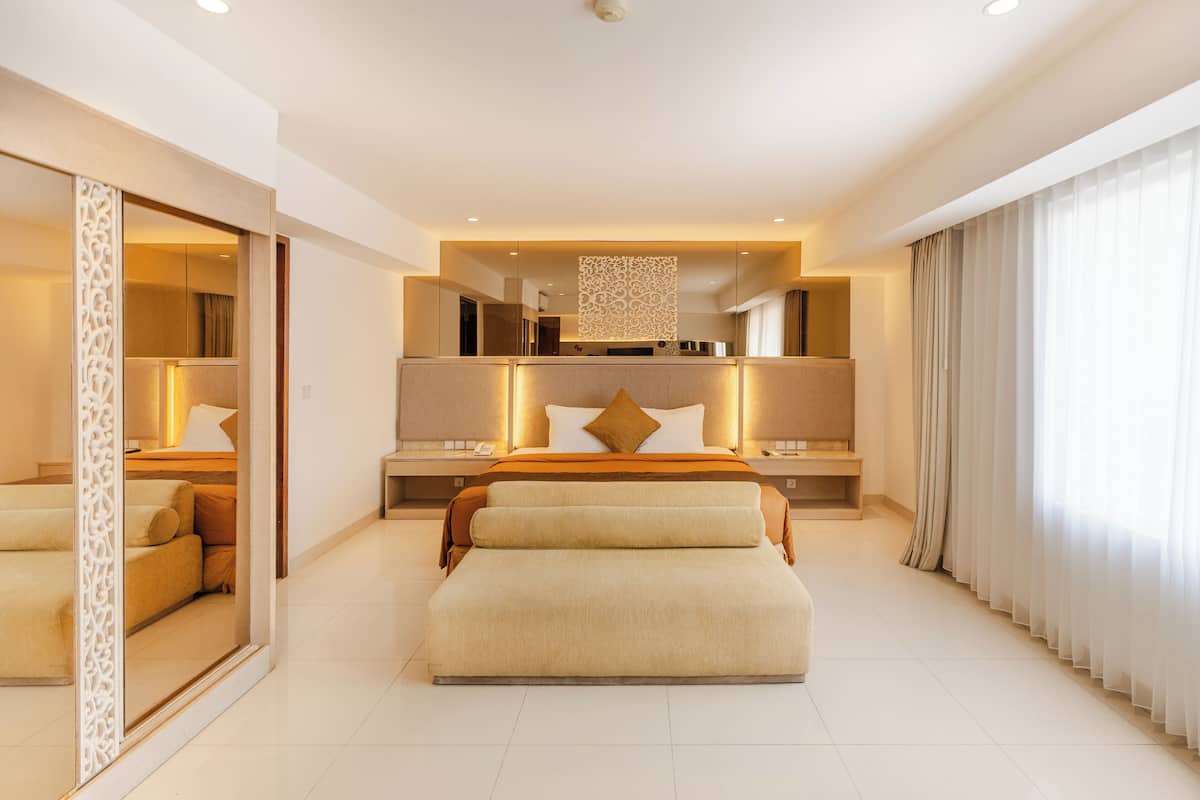 A modern hotel bedroom with a large bed, bedside tables, a mirror, and a view of the outside.