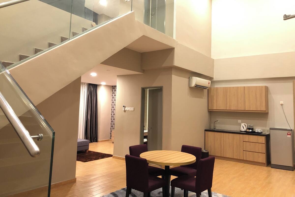 Eine moderne Wohnung mit Treppe, einem Essbereich mit violetten Stühlen, einer Küche mit Holzschränken und einem kleinen Kühlschrank.