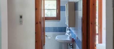 A narrow hallway leading to a bathroom with a sink, a window, and a white air conditioning unit mounted on the wall.
