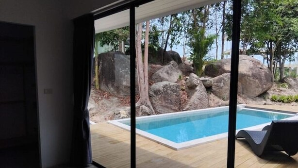 A modern room with a large sliding glass door leading to an outdoor swimming pool area with rocks and trees.