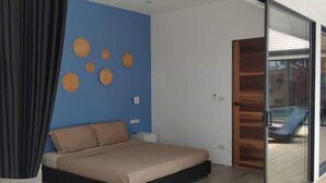 A bedroom with a bed, a nightstand, a blue wall with circular decorations, and a sliding glass door leading to a balcony.