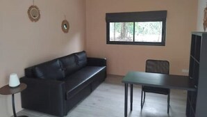 A room with a black leather sofa, a small table, and a window with a view of trees.