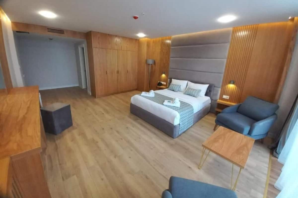 Una habitación de hotel moderna con una cama grande, un área de descanso y paneles de madera.