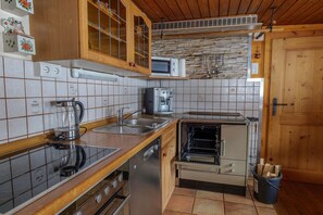 A kitchen with a stove, sink, microwave, and a stone wall backsplash. - Chalet near Passthurn Ski Area Kitzbühel (Mittersill)