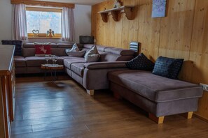 A cozy living room with a brown leather sofa, a wooden coffee table, and a window with curtains.