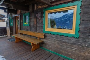 A wooden cabin with a bench, a window with a mountain view, and a door.