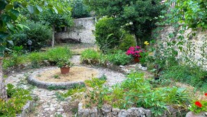 Un jardin avec des murs en pierre, des plantes en pot et un chemin circulaire pavé de pierres.