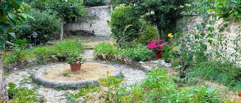 A garden with stone walls, potted plants, and a circular stone pathway.