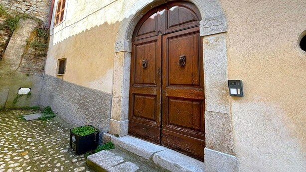 Un bâtiment doté d’un mur en pierre, d’une cour pavée et d’une grande porte en bois à deux battants.