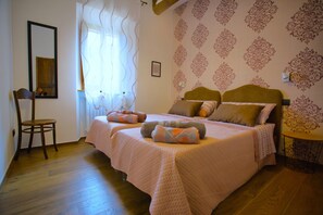 A bedroom with two beds, a chair, a window with curtains, and patterned wallpaper.