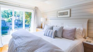 A bedroom with a large bed, a nightstand, a lamp, and a view of the outside.