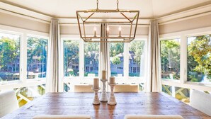 A dining room with a wooden table, white upholstered chairs, and a chandelier.