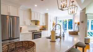 A modern kitchen with white cabinetry, a large island, stainless steel appliances, and a hanging light fixture.
