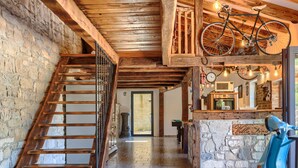 Un interior rústico con una escalera de madera, una pared de piedra, una bicicleta y un patinete.