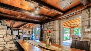 Un comedor rústico con una larga mesa de madera, paredes de piedra y vistas al exterior.