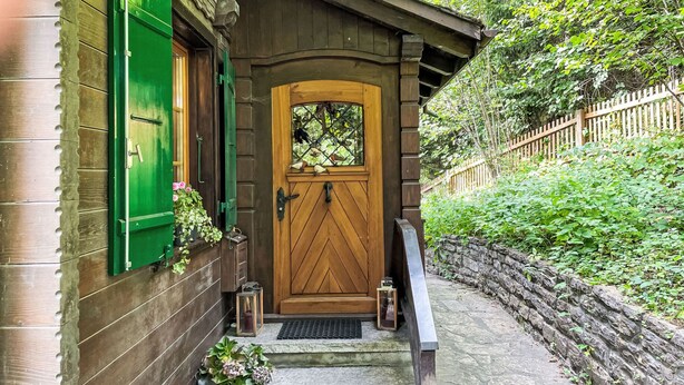 Een houten huis met een groene deur en luiken, een stenen muur en een houten omheining.