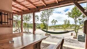 Una veranda esterna con tavoli e panche in legno, un'amaca e vista su alberi e un paesaggio lontano.
