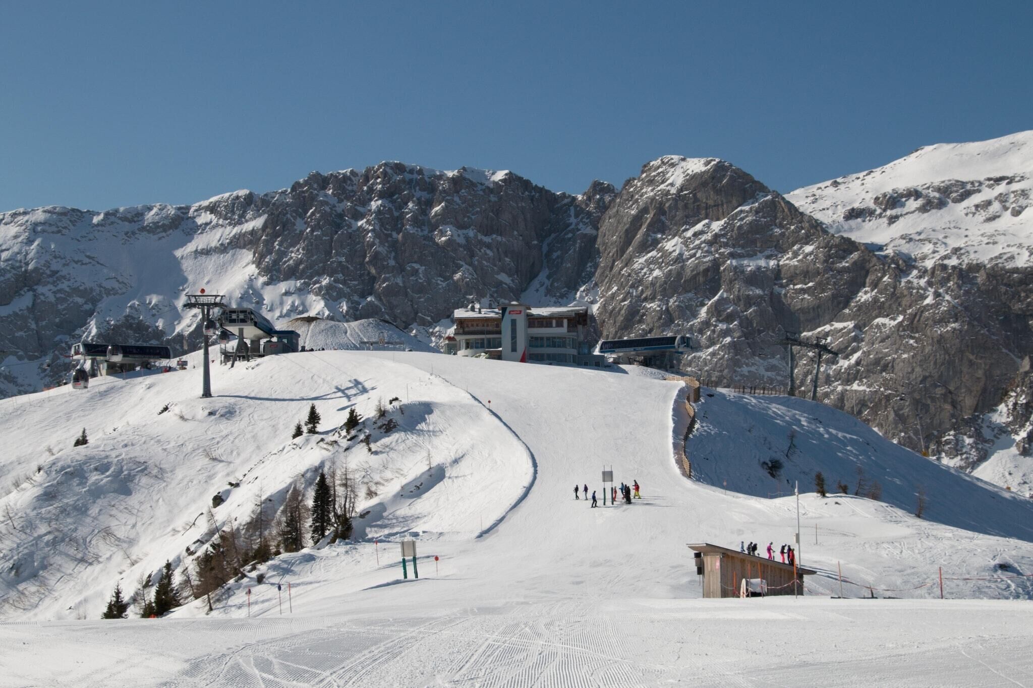 A ski resort with a chairlift, a building with a ski lift, and a snowy mountain backdrop.