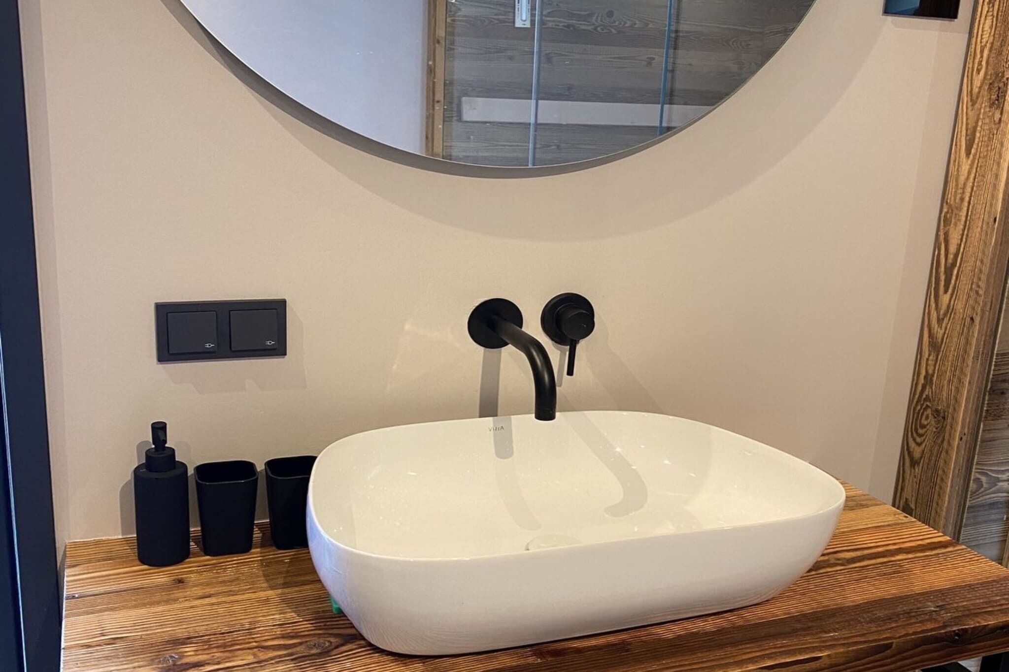 Un baño moderno con un lavabo blanco, un grifo negro y un espejo redondo encima.