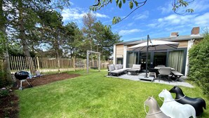Un patio trasero con mobiliario exterior, una parrilla y estatuas decorativas de caballos.