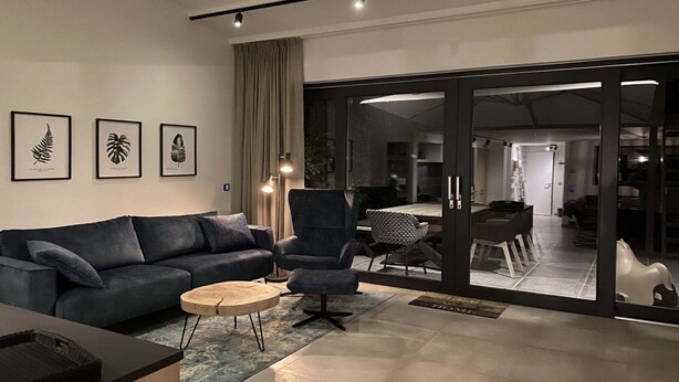 Una sala moderna con un sofá azul oscuro, una mesa de centro redonda y un amplio ventanal corredero que da a un comedor.