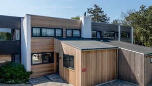 Un edificio moderno de dos pisos con techo plano, ventanas grandes y fachada de madera.