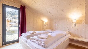 Ein Zimmer in einer Holzhütte mit einem Bett, einem Fenster mit Vorhängen und zwei Wandleuchten.