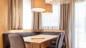 A dining area with a wooden table and chairs, large windows with sheer curtains, and hanging pendant lights.