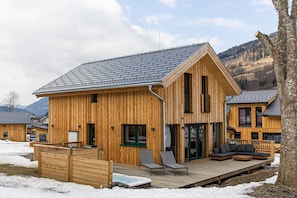 A wooden cabin with a deck, large windows, and a view of mountains.