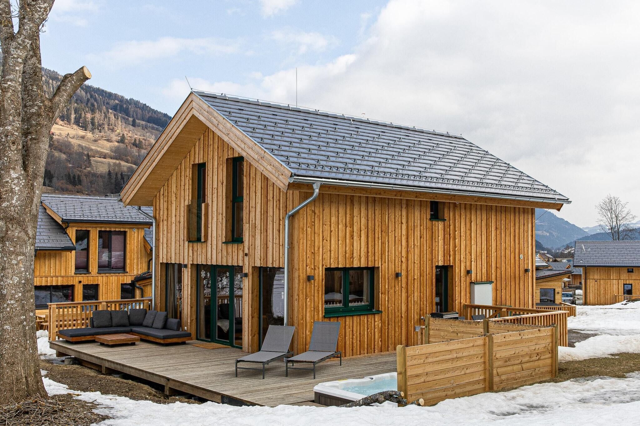 A wooden cabin with a deck, a hot tub, and a view of mountains.