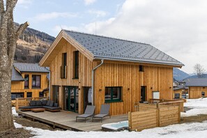 A wooden cabin with a deck, a hot tub, and a view of mountains.