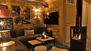 A cozy living room with a stone wall, a fireplace, a sofa, and a flat-screen TV. - Attractive chalet with sauna (Sankt Georgen am Kresichberg)