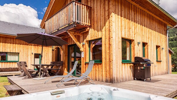 Una cabaña de madera con jacuzzi, mobiliario de exterior y una parrilla.