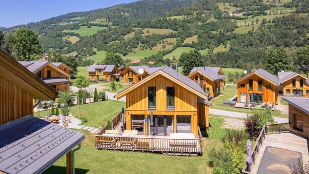 A row of wooden cabins with balconies, set in a green valley with hills in the background. - Beautiful chalet with sauna (Sankt Georgen am Kresichberg)
