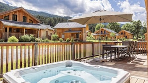 A wooden cabin with a hot tub on a deck, surrounded by other cabins and a mountain backdrop. - Beautiful chalet with sauna (Sankt Georgen am Kresichberg)