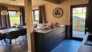 A modern kitchen with a central island, wooden cabinets, and a large clock on the wall. - Beautiful chalet with sauna (Sankt Georgen am Kresichberg)