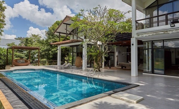 A modern house with a swimming pool, outdoor seating, and a covered patio area.