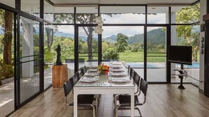 Un comedor con una mesa dispuesta para seis personas, ventanas amplias que ofrecen vistas a un paisaje exuberante y una piscina.