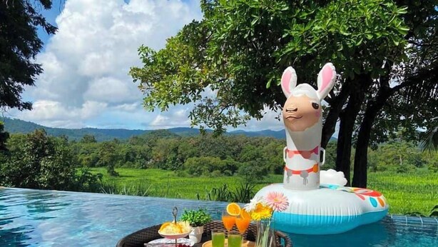 Escena junto a la piscina con una mesa flotante, una figura decorativa de conejo y una vista panorámica de un paisaje exuberante.