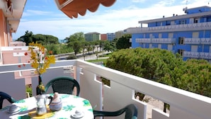 A balcony with a table set for two, a vase with flowers, and a view of buildings and trees.