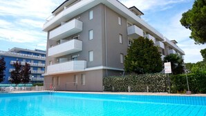 A modern multi-story building with balconies, a swimming pool, and a clear sky.