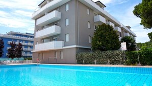 A modern multi-story building with balconies, a swimming pool, and a hedge. - Apartment in Porto Santa Margherita (Porto Santa Margherita - Caorle)