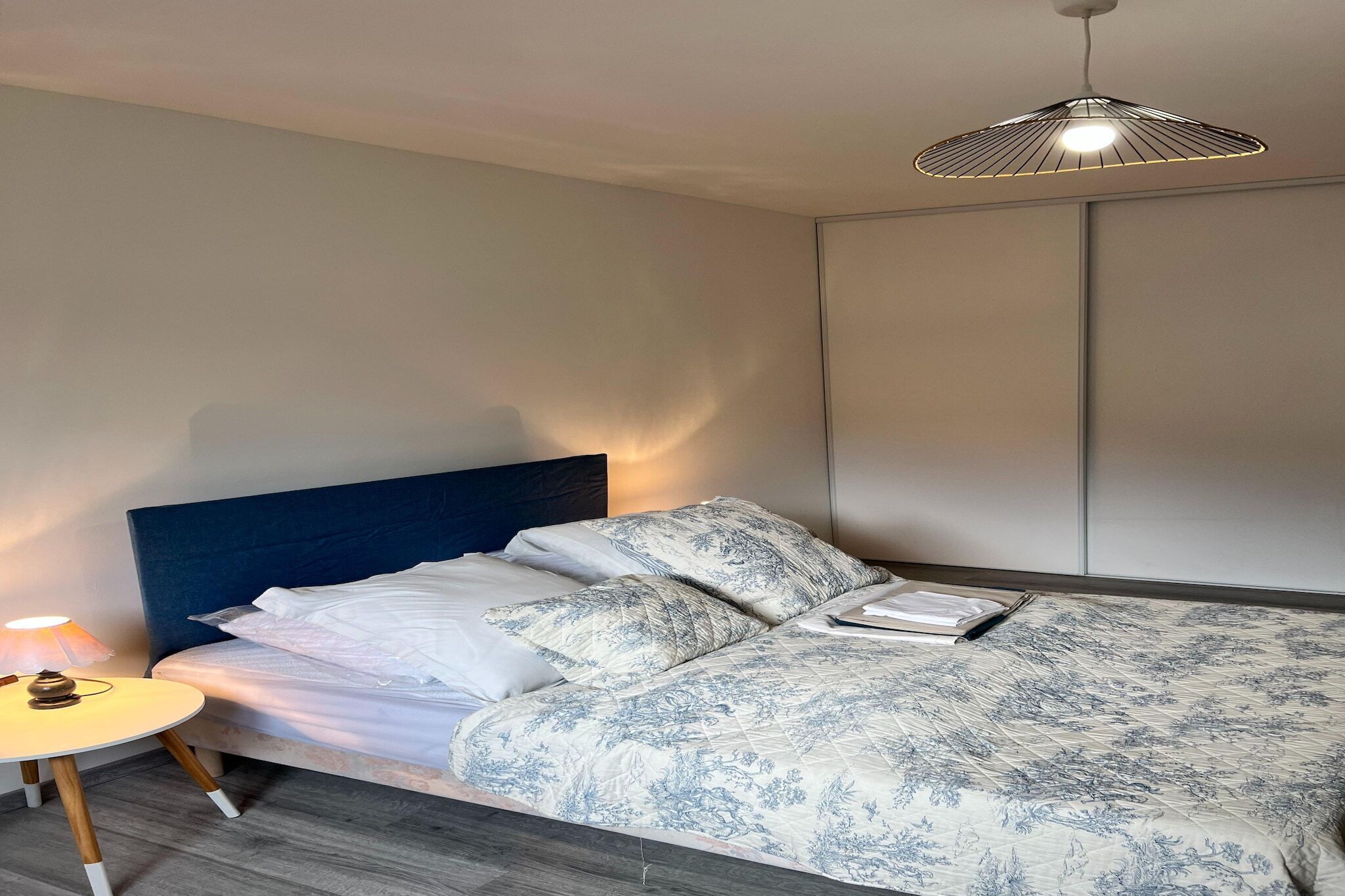 Ein ordentlich bezogenes Bett mit einem gemusterten Duvet, einer Nachttischlampe und einer hängenden Leuchte.