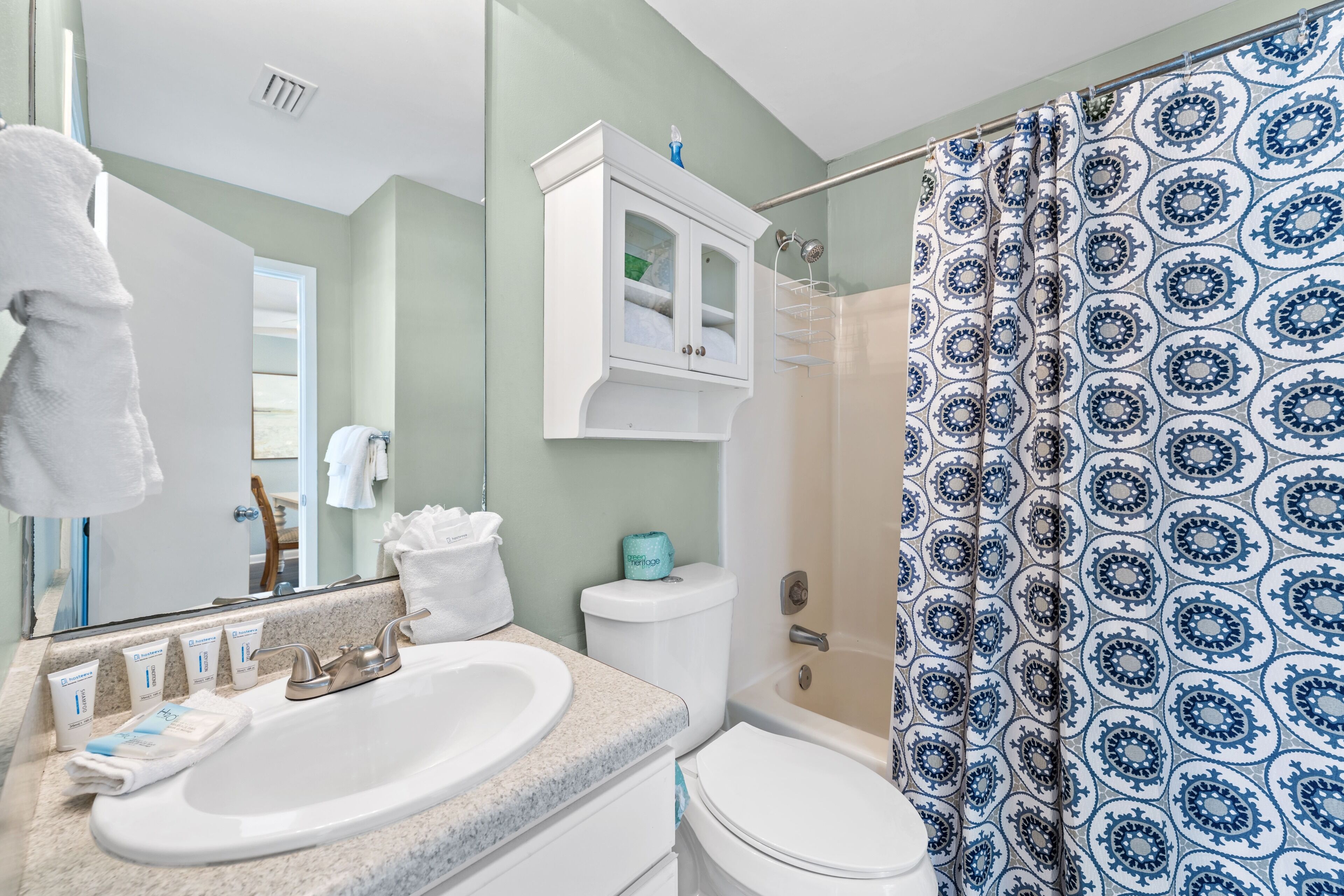 A bathroom with a sink, mirror, toilet, and shower curtain.