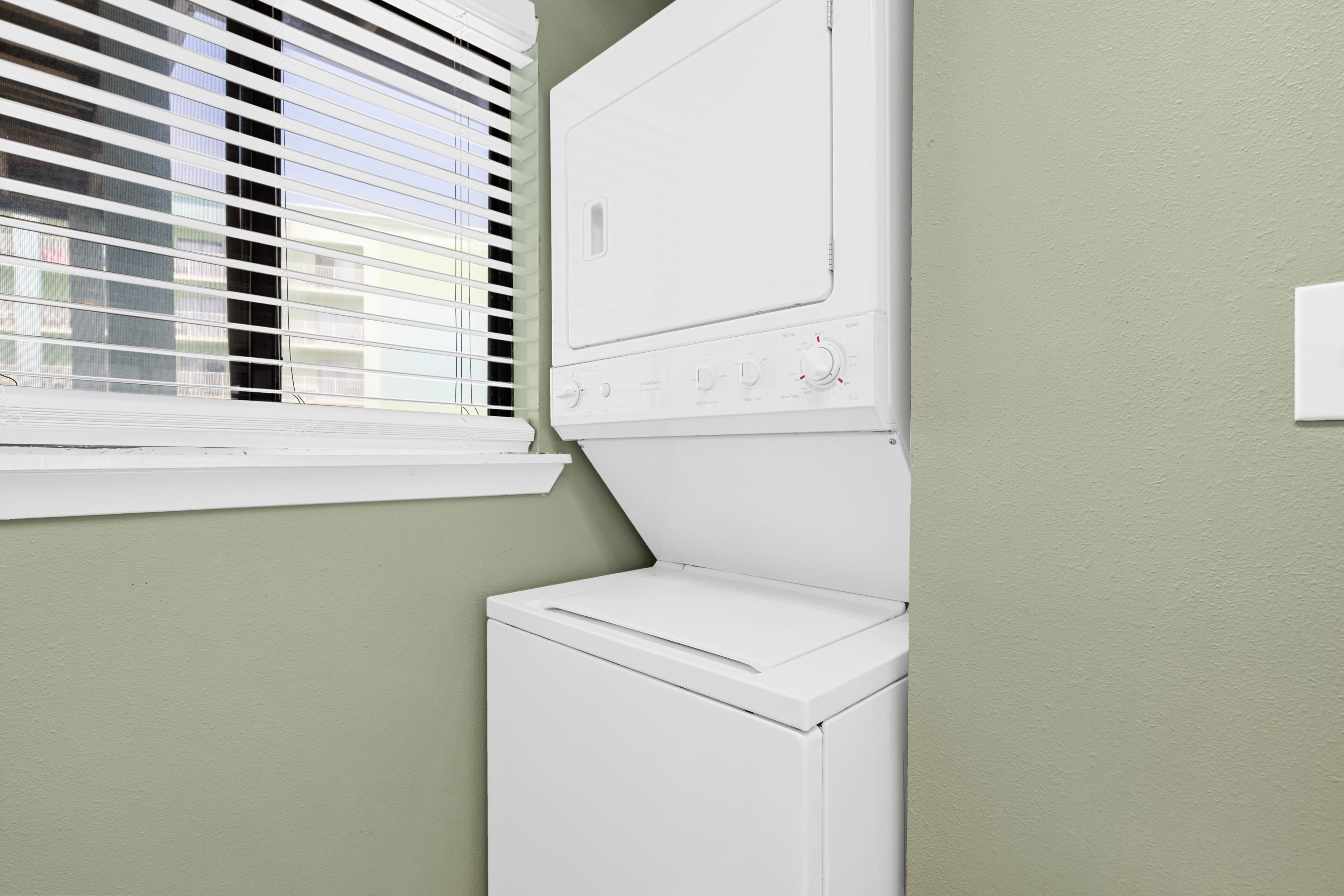A laundry room with a washer and dryer, a window with blinds, and a light switch on the wall.