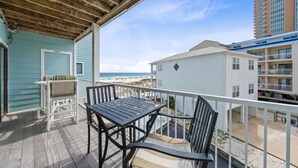 A wooden deck with a table and chairs, overlooking a beach and a multi-story building. - Romar Beach 203 (Orange Beach)
