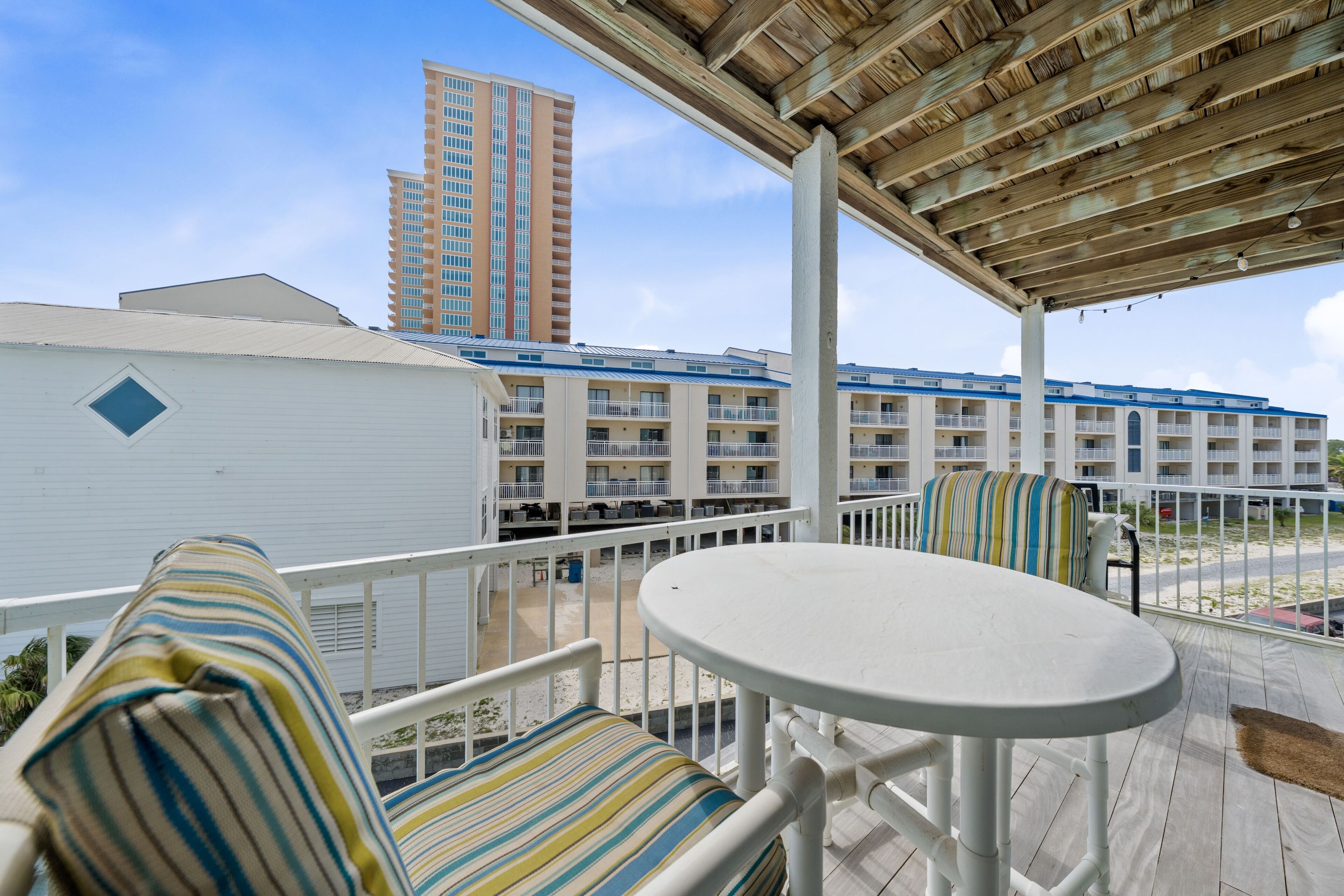 Ein Balkon mit gestreiften Kissen, einem weißen Tisch und Blick auf ein mehrgeschossiges Gebäude.