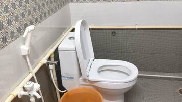 A small, enclosed bathroom with a toilet, a handwashing station, and a bucket.